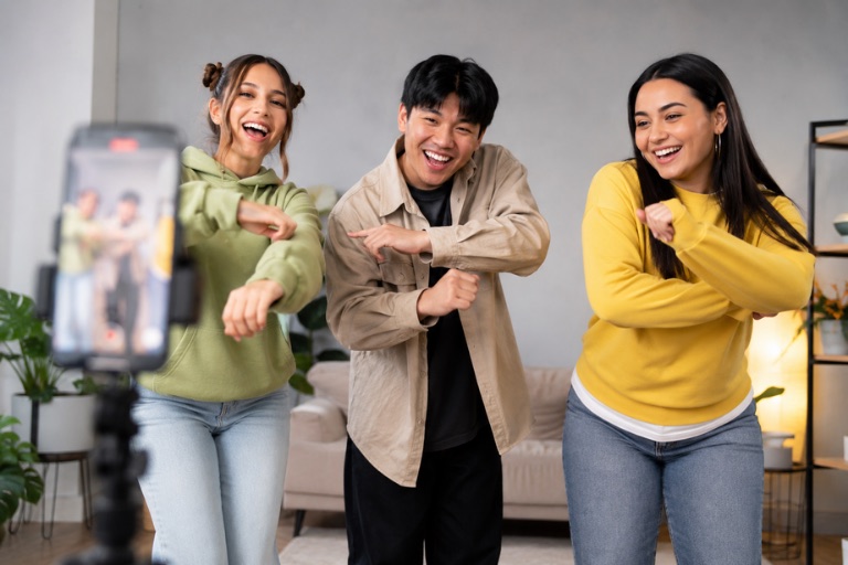 Three friends dancing together while filming a TikTok video on a tripod-mounted phone