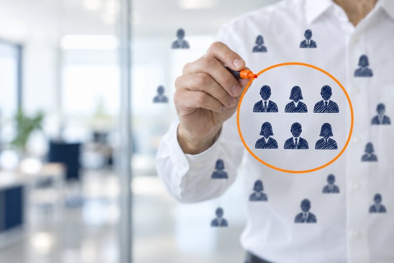 A hand drawing an orange circle around one group of people among a crowd, illustrating selecting a specific audience segment