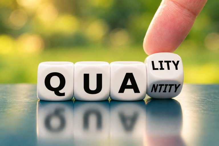 Lettered dice spelling the word quality, with a finger turning the last die from quantity to quality
