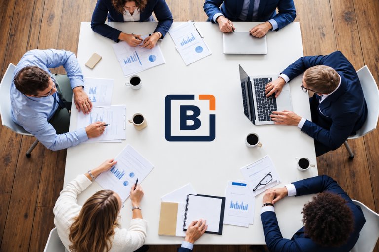 An overhead view of six colleagues working through printed performance charts around a table centered with the Brill Media logo